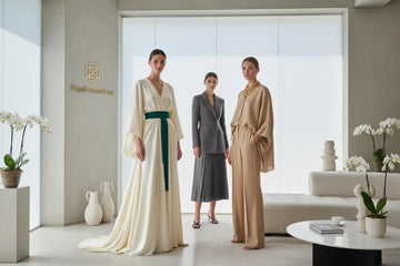 Three models showcase trendy clothing featuring stylish minimalist dresses and versatile tops in a bright showroom.