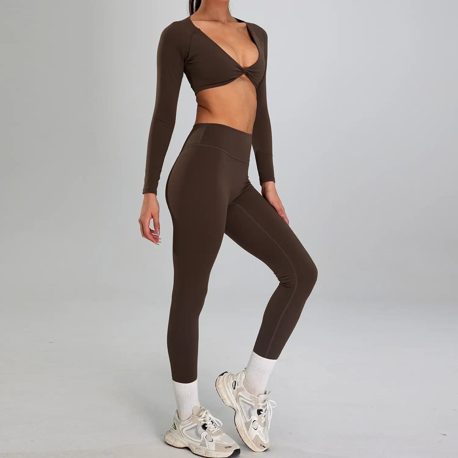 A sleek chocolate-brown two-piece sports suit outdoor featuring a long-sleeved crop top with twisted front detail and high-waisted stretchy leggings suitable for outdoor running nude activities.
