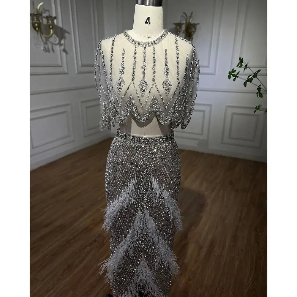 Silver nude two-piece evening dress featuring silver beaded fabric, feather accents, and a sheer embellished bodice ideal for formal occasions.