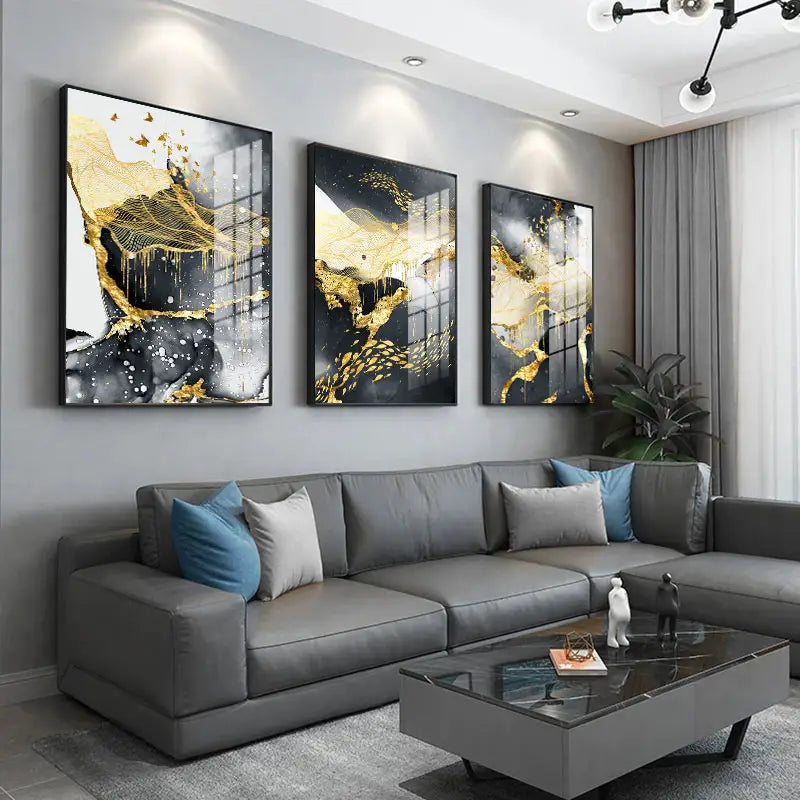 three framed golden black abstract wall art posters with white splashes hang above a gray sectional sofa as white wall art.