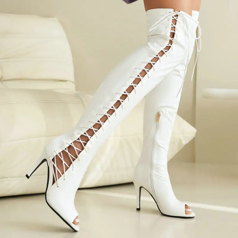 White patent leather female over the knee boots with lace up detailing along the side, peep toe design, and high heel height.