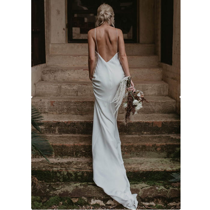white satin evening gown shown from the back with a deep cutout, delicate spaghetti straps, and a flowing train brigade shot long silhouette