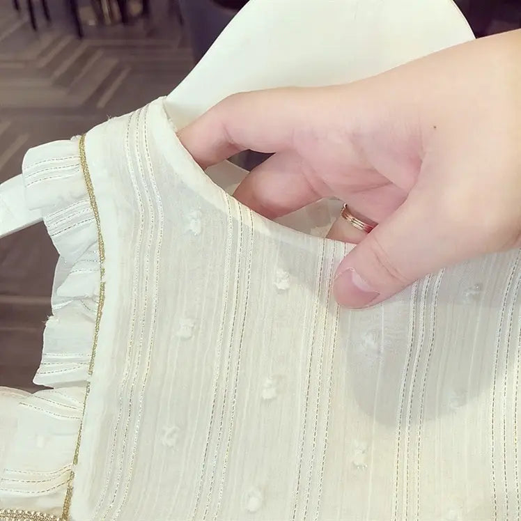 A delicate off-white baby gauze dress summer princess dress featuring subtle vertical ribbing, tiny embroidered flowers, and fine gold thread trim along the ruffled neckline.