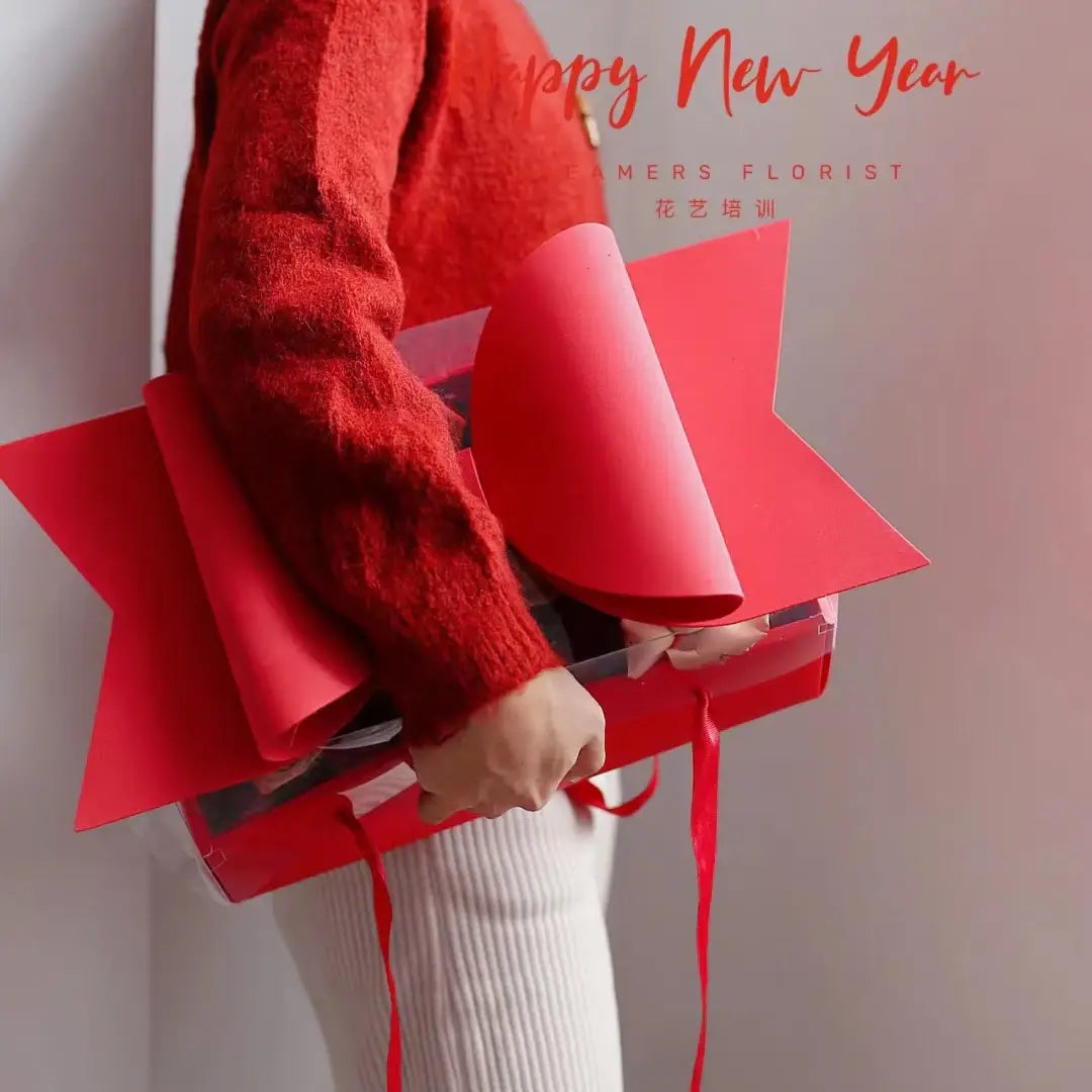 Red bow knot handheld flower box is a red star-shaped gift box with a clear plastic front and red ribbon handles.