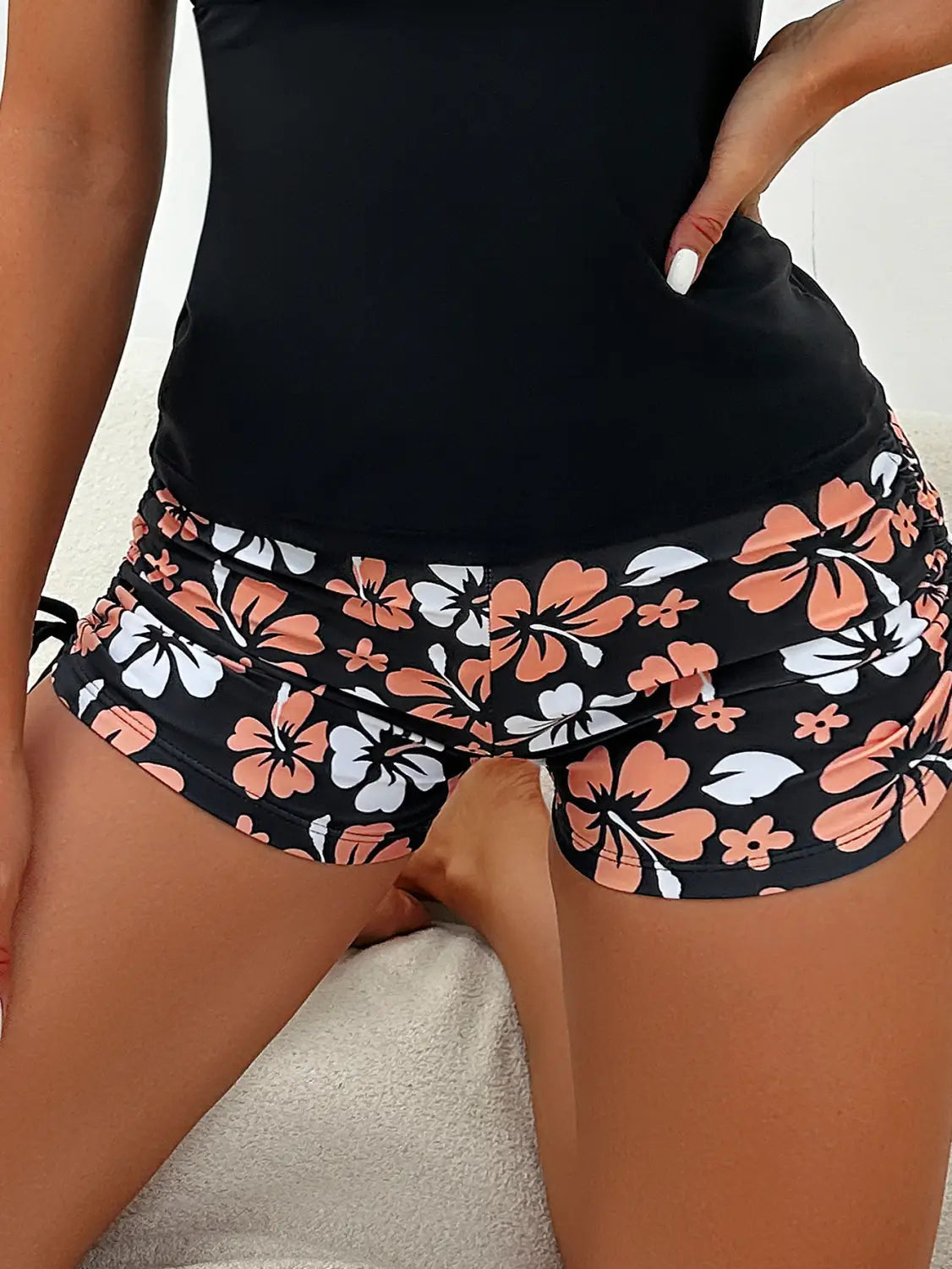 Black shorts with a vibrant floral pattern featuring peach and white hibiscus flowers as part of a floral halterneck printed halter split swimsuit.