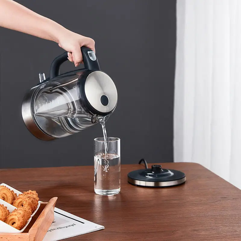 Small glass electric kettle with a black handle and stainless steel lid being poured into a glass with red LED light indicator.