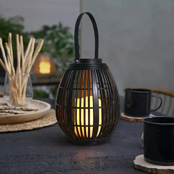 Black wrought iron lantern with a warm glowing led candle inside designed as a black solar retro patio woven rattan lantern.