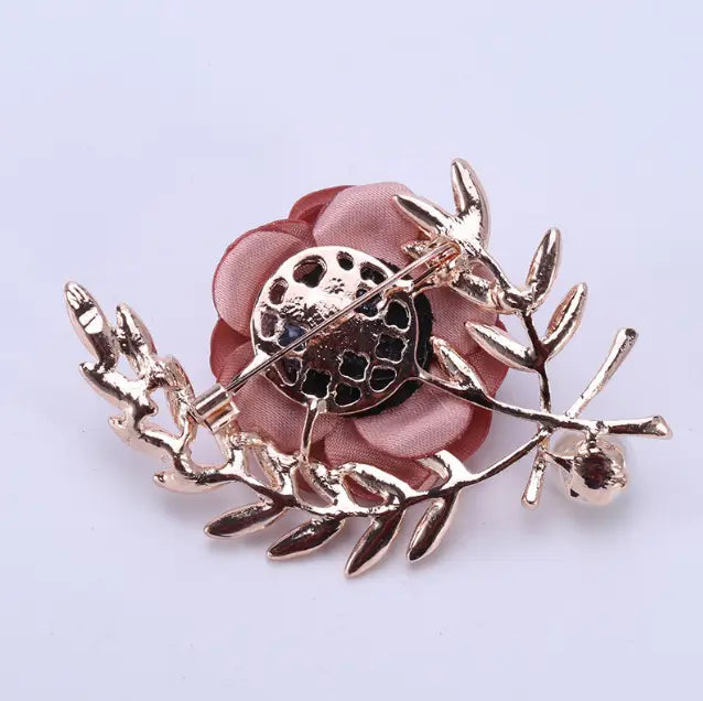 a delicate fabric flower lady temperamental pin featuring pink fabric petals shaped like a rose and a metallic gold-tone leaf design.