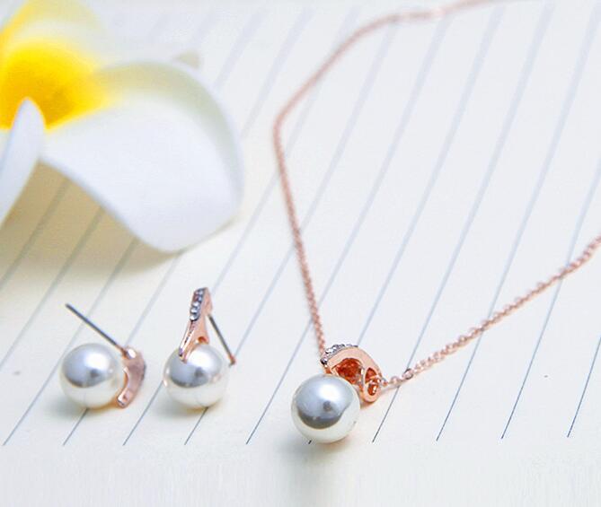 Rose gold bride rhinestone pearl earrings necklace set featuring a single pearl pendant necklace and matching stud earrings accented by tiny diamonds.