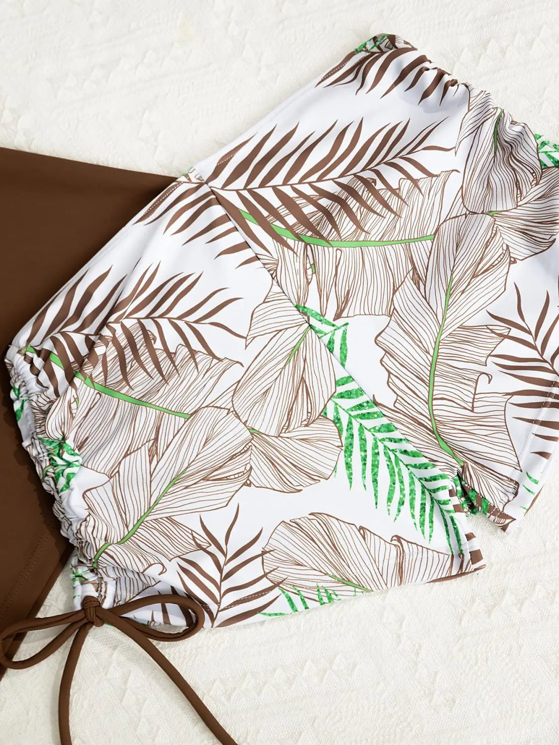 white bikini bottom with tropical brown and green leaf pattern elasticated waistband and drawstring ties as part of a floral halterneck printed halter split swimsuit
