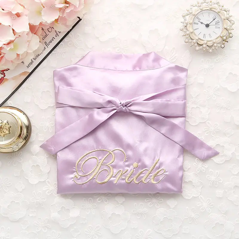 A lavender satin bridal pajamas simulation silk robe with gold embroidered lettering and a matching ribbon tie for a simulation silk nightgown.