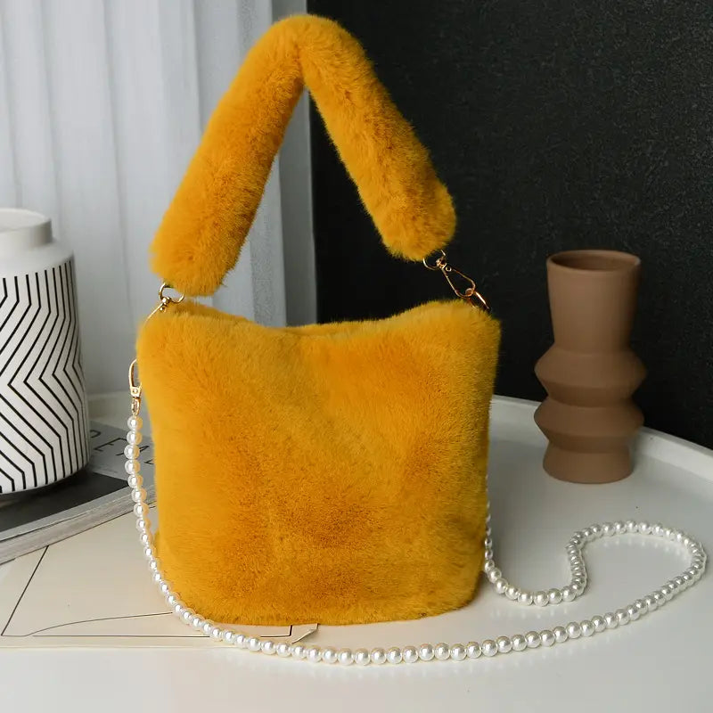 A vibrant yellow checkerboard plush bucket bag featuring soft faux fur material with a matching fluffy handle and a detachable pearl chain design.