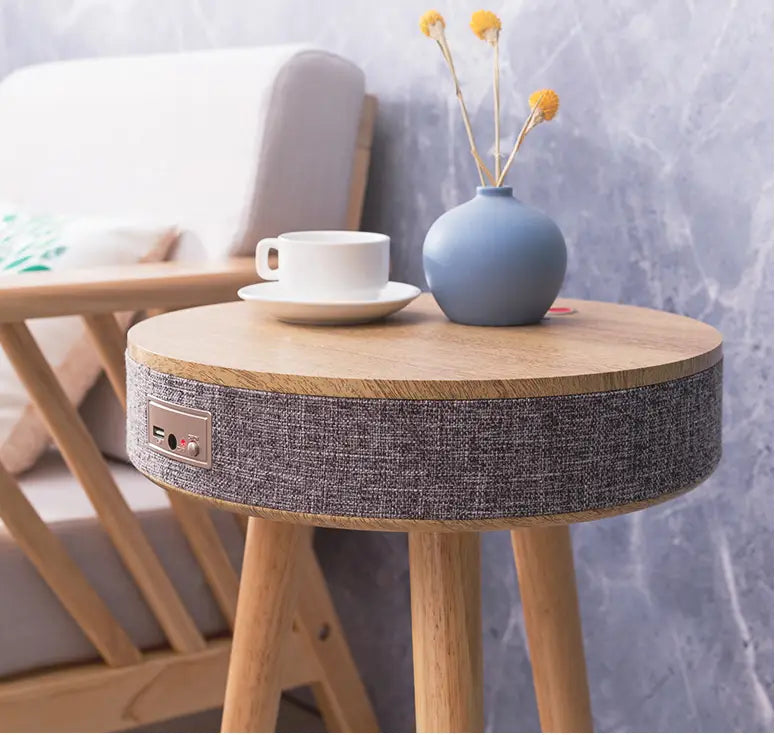 Round wooden smart side table in log color with gray textured fabric wrap featuring integrated smart voice speaker controls and wireless charging functionality.