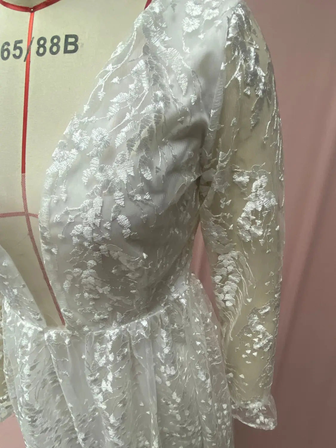 A delicate white long sleeve wedding dress lace gown with intricate floral embroidery and sheer sleeves displayed on a mannequin.