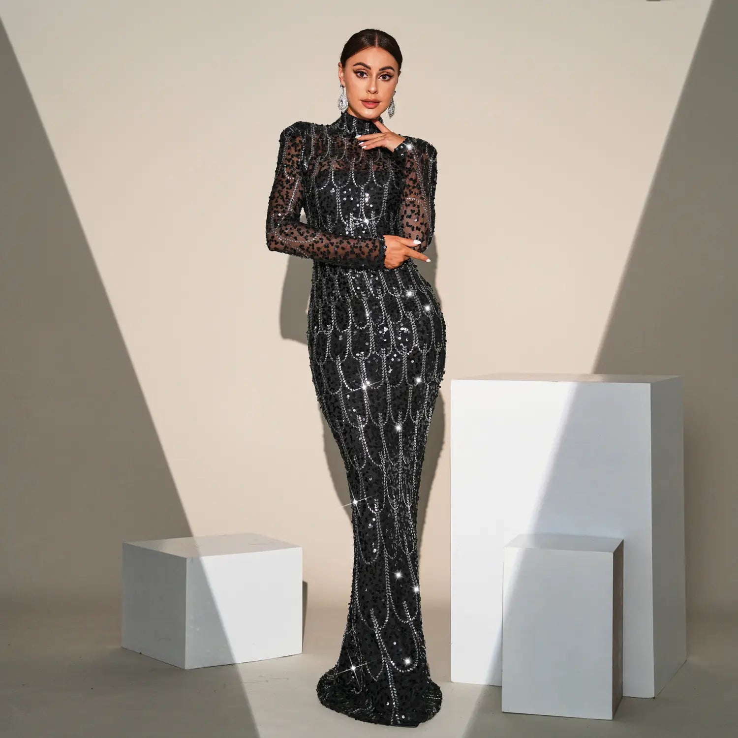 A black sequined banquet evening gown with long sleeve round neck sheer sleeves and intricate silver chain detailing cascading down the bodice and skirt.