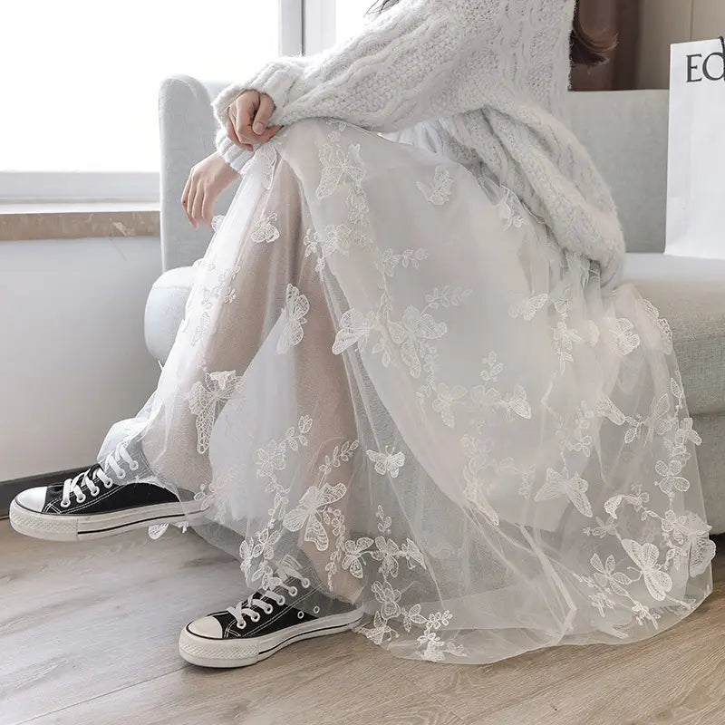 a flowing mid-length white lace mesh skirt featuring embroidered bow lace detailing with delicate butterfly and floral patterns