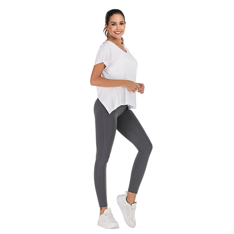 A woman wearing a white v-neck sports t-shirt with an open back and dark gray form-fitting leggings.