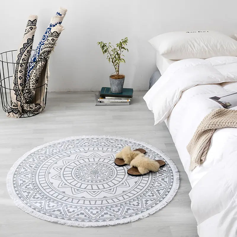 Navy mandala ethnic style round carpet floor mat with intricate gray geometric patterns and white fringe placed on light wood flooring.