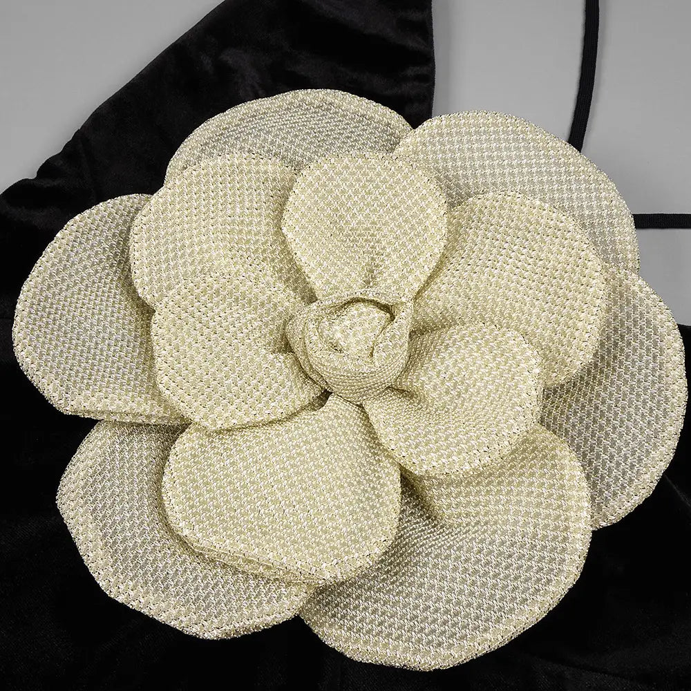 a cream-colored textured fabric flower accessory with layered petals on a black camisole backless slim fit velvet floral gown