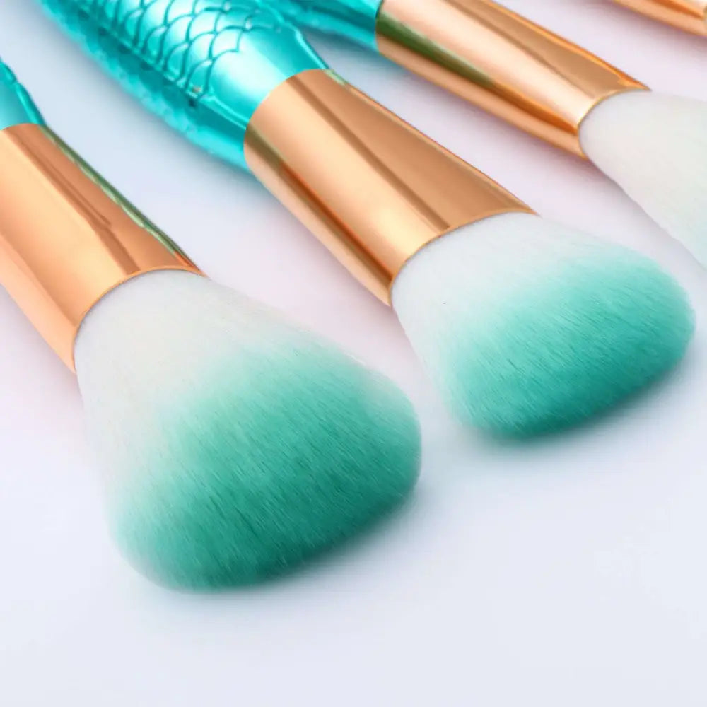 Set of three teal and rose gold mermaid makeup brushes with gradient green bristles from 11pcs brushes kit featuring palette