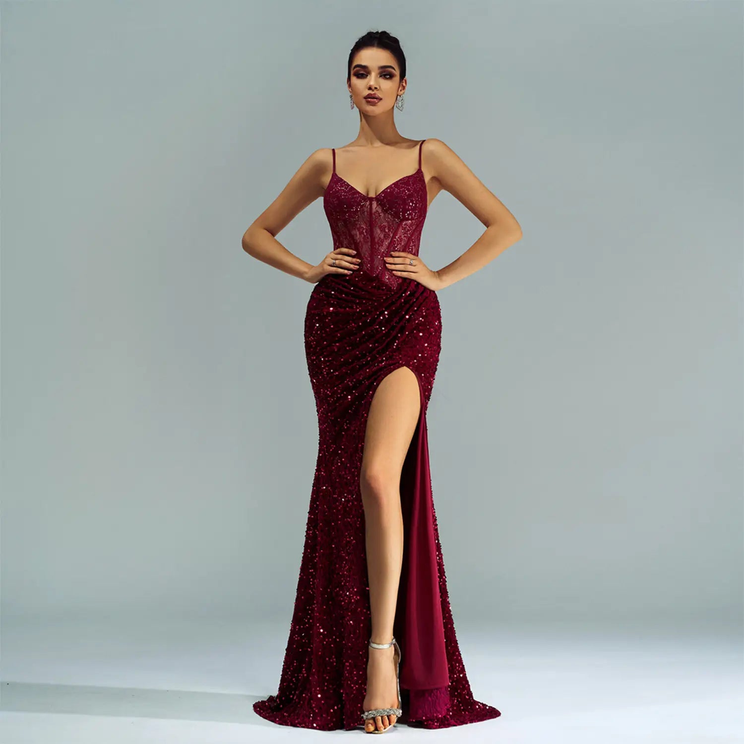 A shimmering burgundy sleeveless sequined high slit evening dress with a fitted bodice and spaghetti straps.