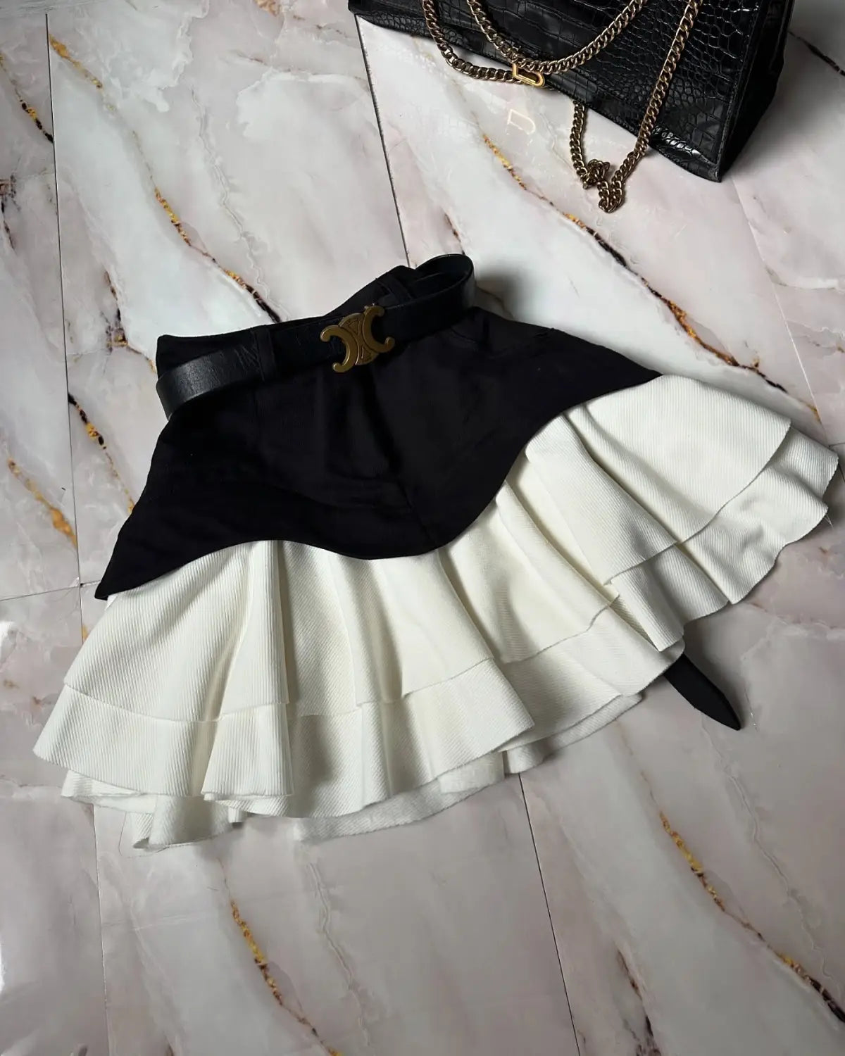 black and white two-tone pleated waist tiered skirt with a black belt featuring a gold-toned c-shaped buckle suitable as a ruffled high waist garment