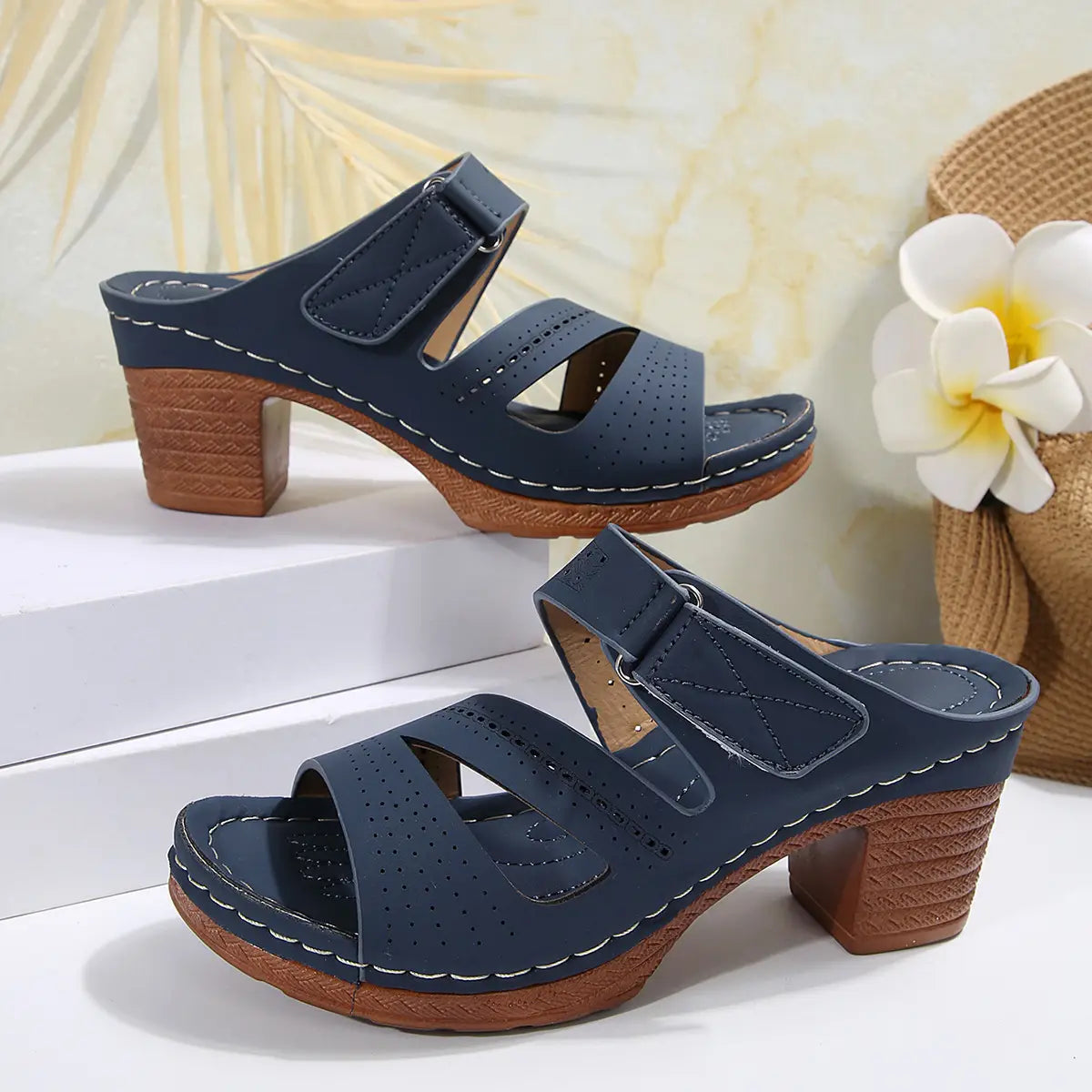 Navy blue perforated leather mule sandals with textured wooden block heel and white stitching designed as summer casual chunky shoes.