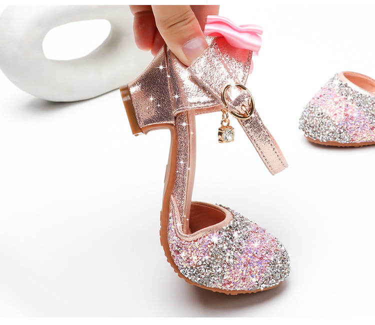 A sparkling rose gold and silver glittery girls high heel summer sandal with a pink bow accent and rhinestone embellishments.