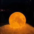 Glowing orange 16-colour remote control moon night table lamp with detailed moon surface texture on a fluffy white base