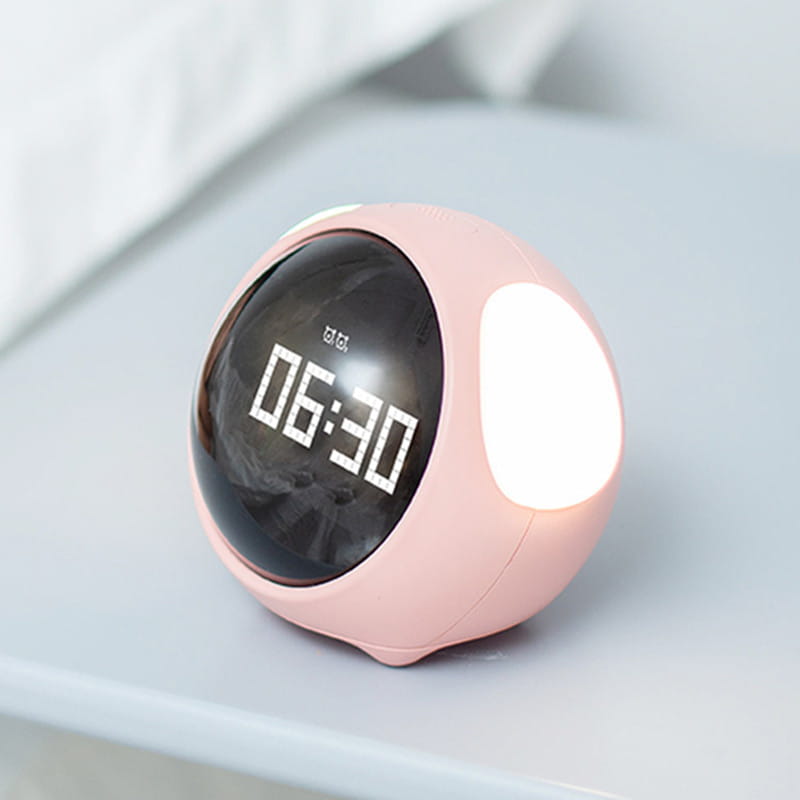cute pixel expression digital electronic alarm clock in pink spherical design with black display showing 06 30 and glowing white light on the side