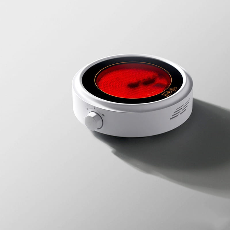 White ceramic electric earthenware oven hot plate with a glowing red heating element and black rim.