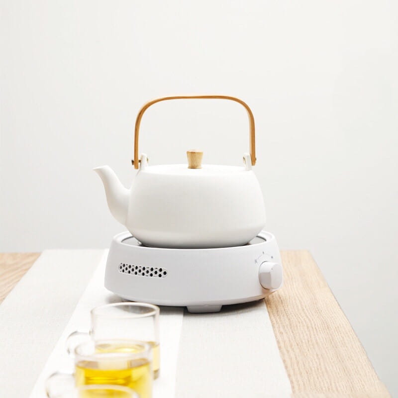 white ceramic electric earthenware oven featuring a teapot with a gold-toned handle and lid knob resting on a matching white electric kettle warmer