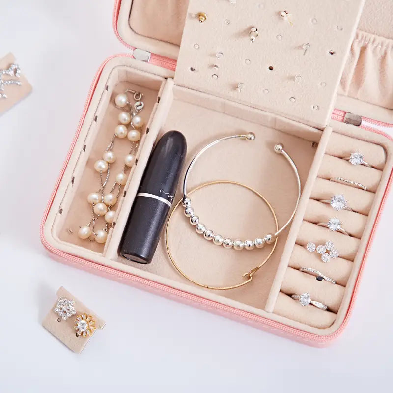 pink velvet-lined multifunctional jewelry storage box with mirror featuring compartments holding pearl necklaces gold bangles diamond rings and a black mac lipstick for organized jewelry storage.