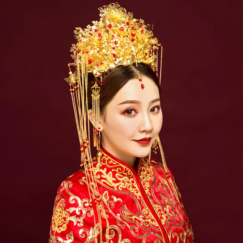 golden ornate wedding chinese xiuhe headdress with ear clip adorned with red gemstones and dangling chains displayed in a gift box.