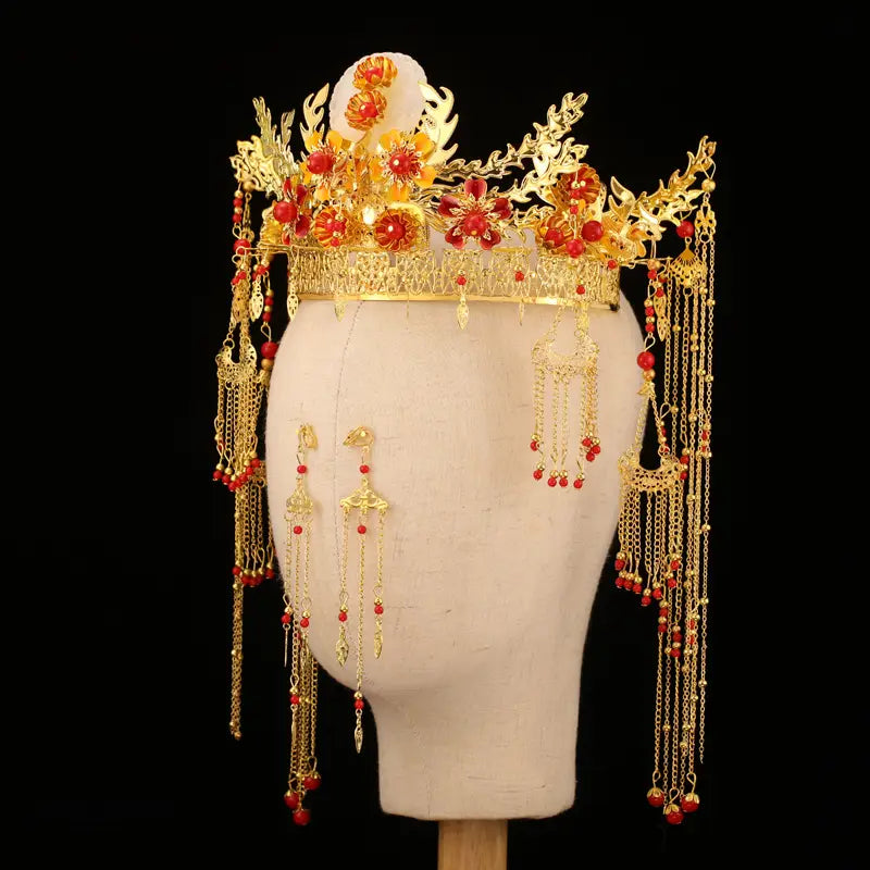 Golden ornate wedding chinese xiuhe headdress with ear clip featuring red and orange floral embellishments intricate filigree work dangling chains and bead accents displayed with gift box.