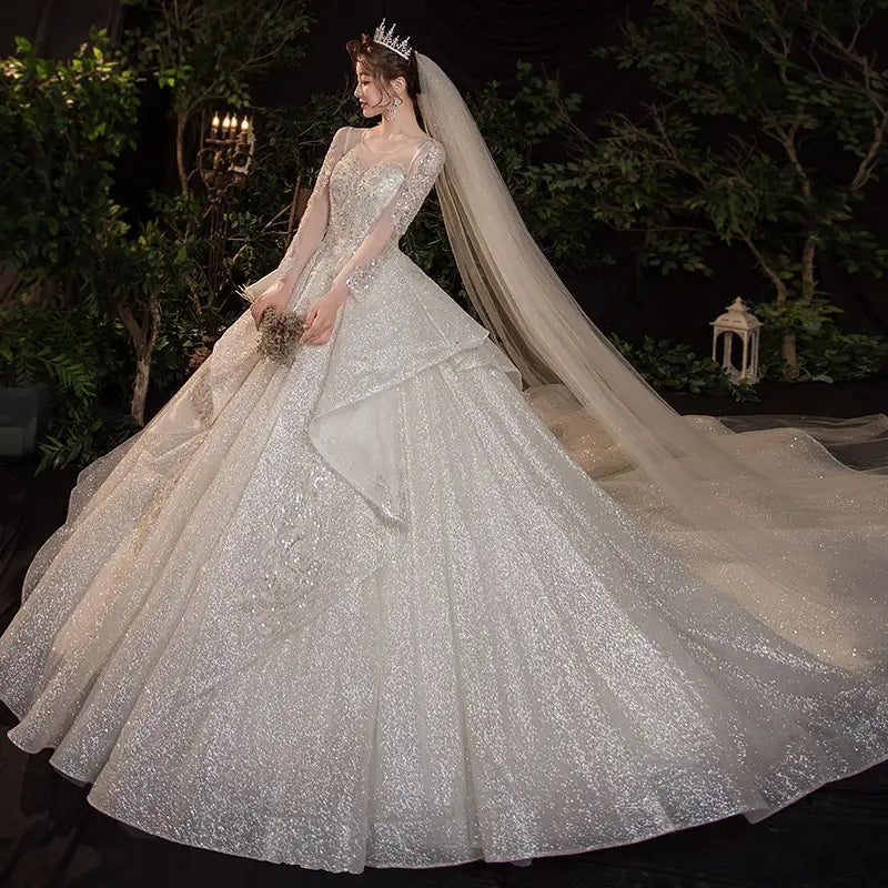 a shimmering white wedding evening dress with long sheer sleeves and a voluminous skirt adorned with sparkling sequins from the bride french temperament dream collection