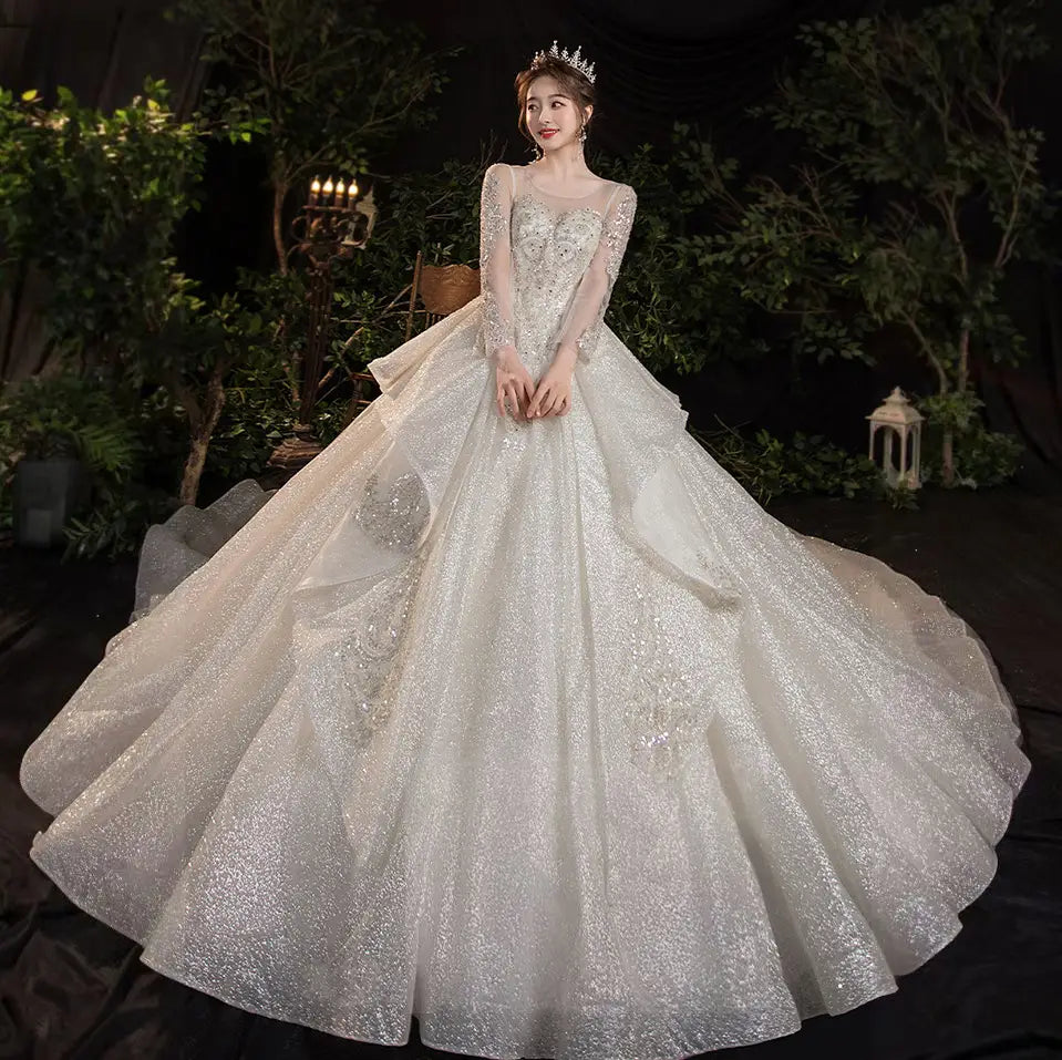 A shimmering white wedding evening dress with long sheer sleeves, intricate beading, and a voluminous skirt made of glittery tulle from the French Temperament Dream collection.