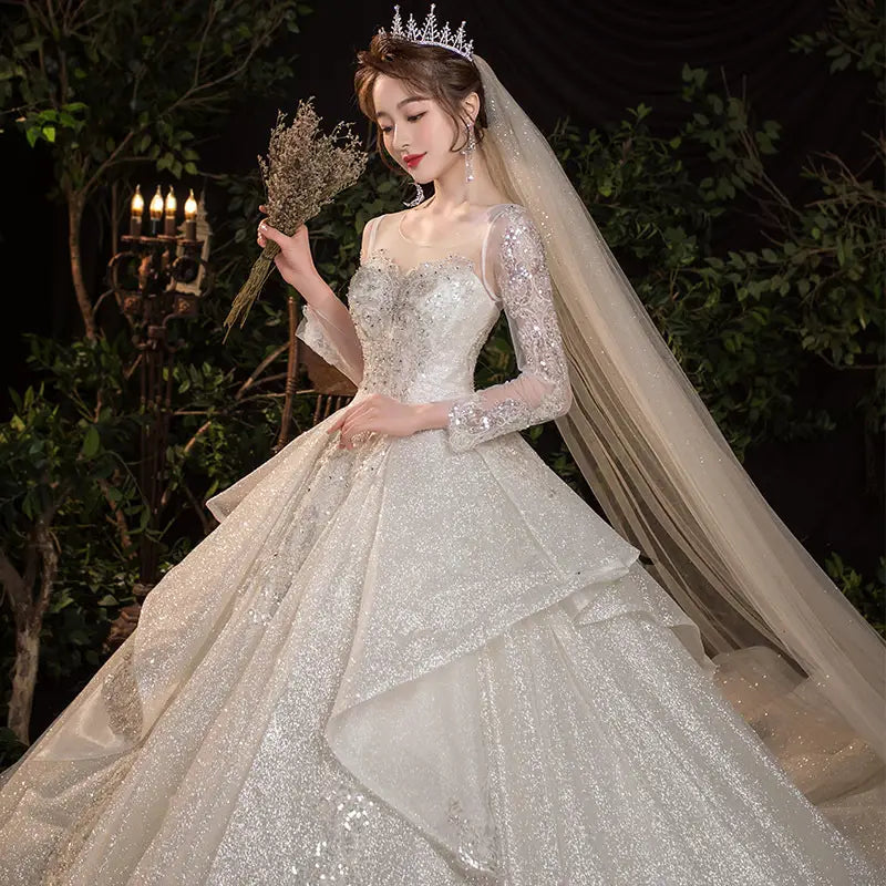 A sparkling white wedding evening dress from the French temperament dream collection featuring long sheer sleeves and a tiered glittering skirt ideal for the bride french temperament.