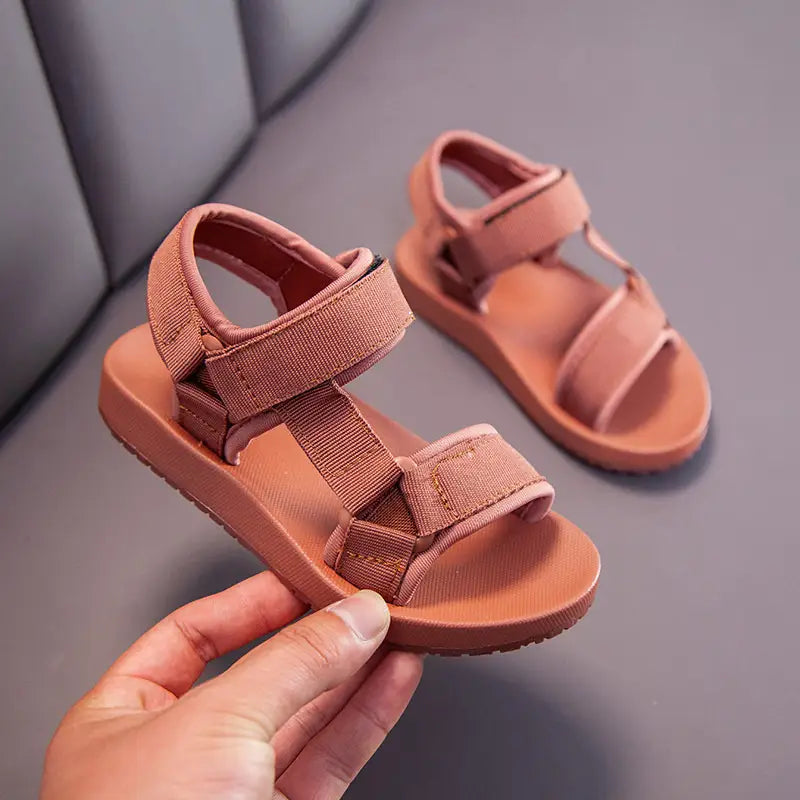 A pair of soft peach-colored children’s school breathable casual sandals with adjustable velcro straps and a cushioned rubber sole.