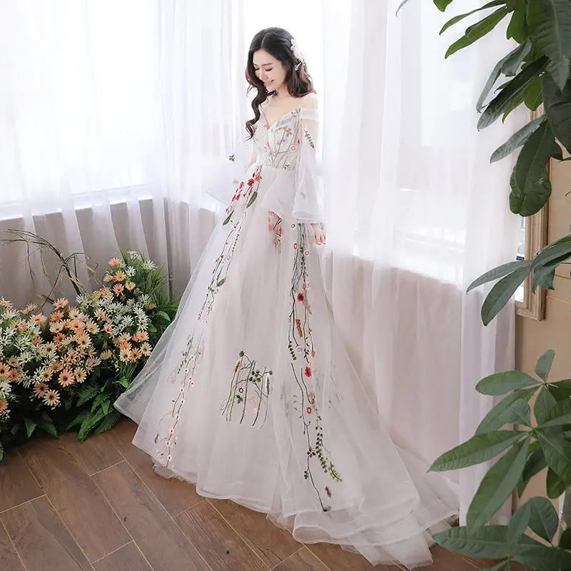 A flowing white gray tulle wedding dress features delicate red green and black floral embroidery in a retro bridal gown style.