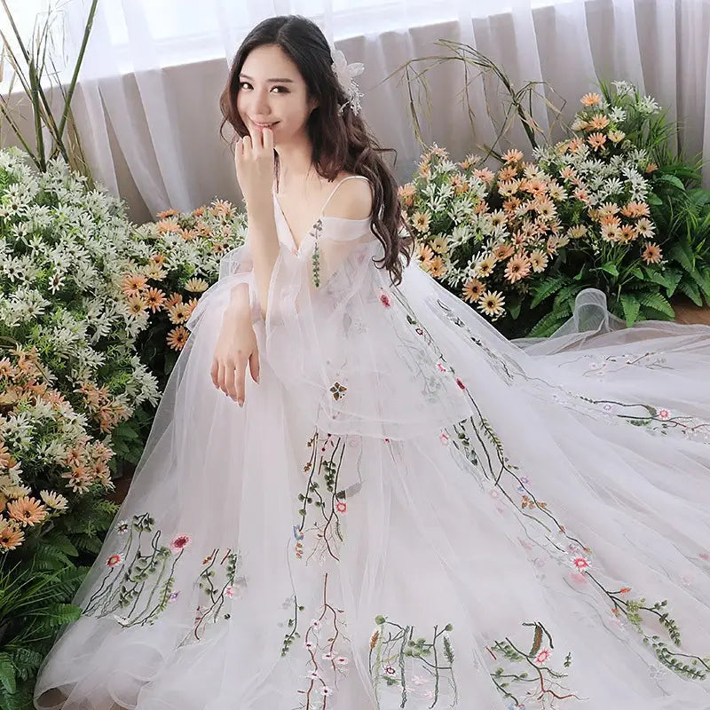 A flowing white tulle wedding dress featuring delicate floral embroidery in soft pink green and black hues perfect as a retro bridal gown.