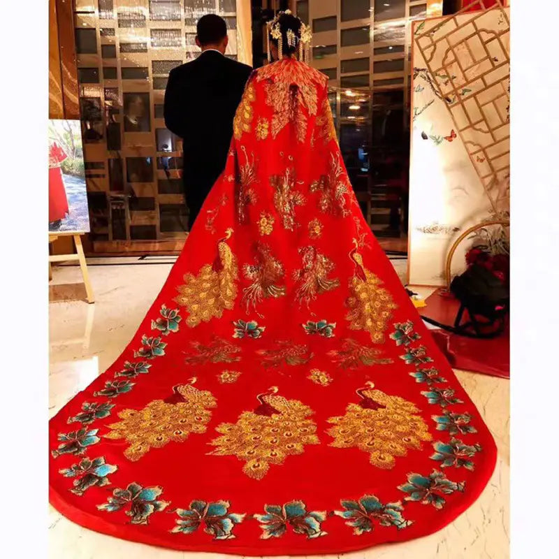 a vibrant red ancient xiuhe dress tailing featuring a big cloak with intricate gold and teal peacock embroidery and a flowing train