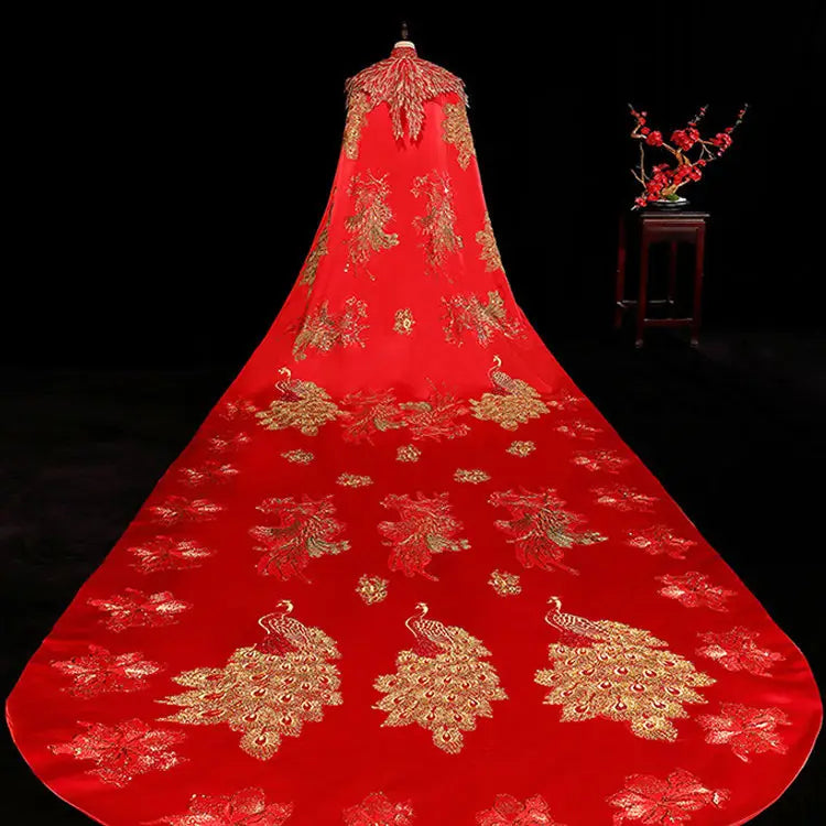 a vibrant red ancient xiuhe dress tailing featuring a big cloak with intricate gold peacock and floral embroidery made of luxurious satin-like fabric