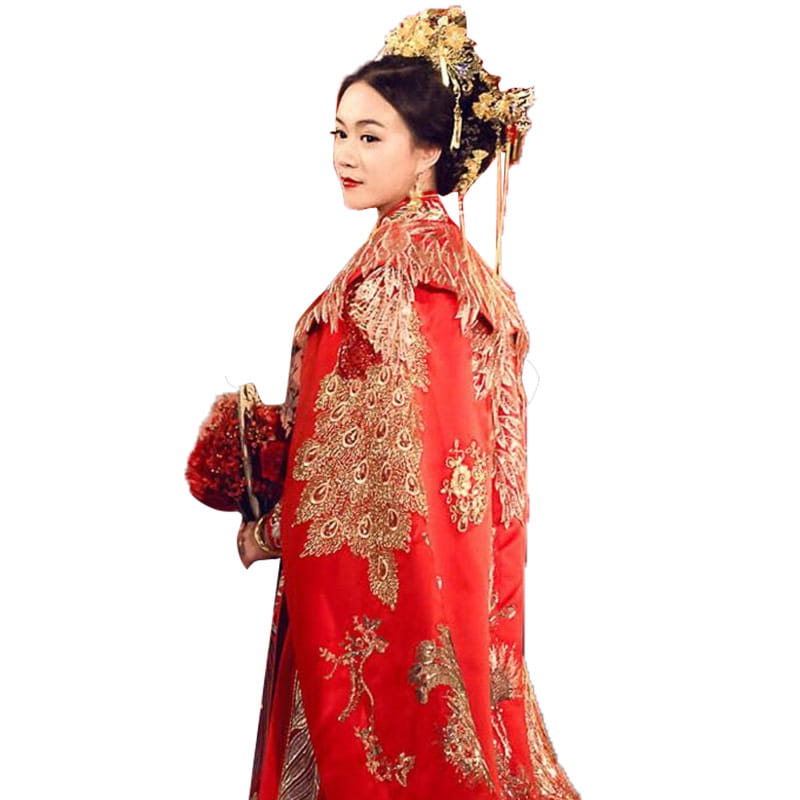 A woman wears a vibrant red ancient xiuhe dress tailing featuring intricate gold embroidery with peacock and floral motifs and a big cloak.