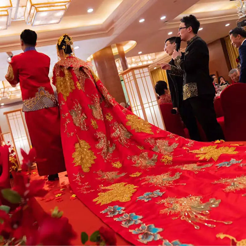 a vibrant red ancient xiuhe dress with intricate gold and blue embroidered phoenixes and floral patterns featuring a long trailing train and a big cloak, shown from the back side of the xiuhe dress tailing