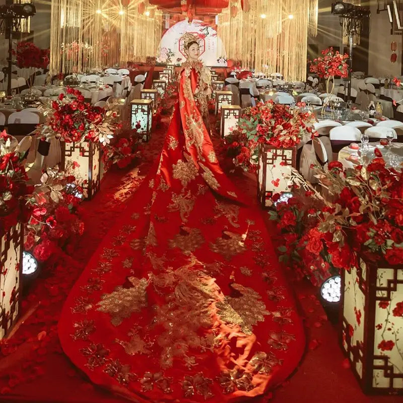 A woman wearing an ancient xiuhe dress in vibrant red with intricate gold embroidery and a big cloak flowing in the xiuhe dress tailing style.