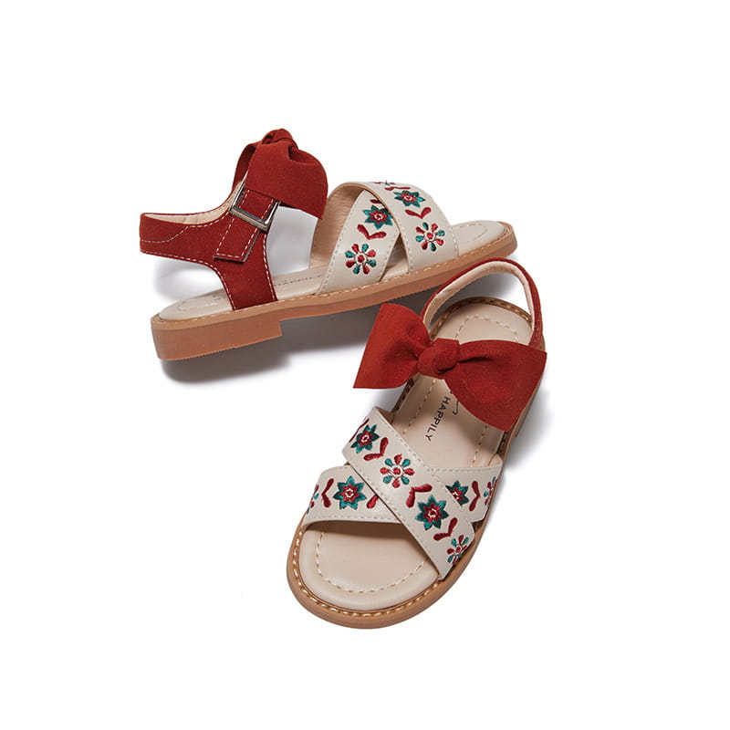 Cream-colored big children’s soft-soled sandals featuring red suede bows and floral embroidery on the straps.