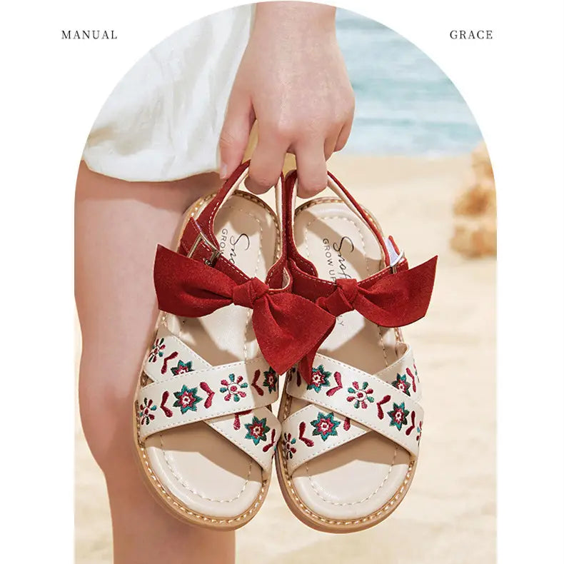 white big children’s soft-soled sandals with red and green floral embroidery and a large red bow on the strap designed as baby children’s shoes