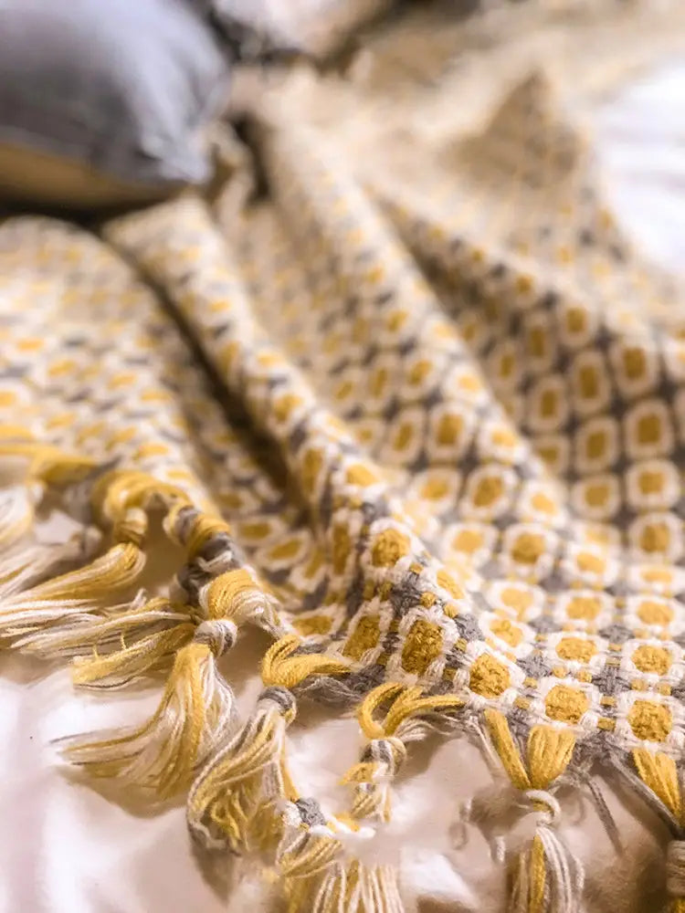 A cozy mustard yellow and gray geometric knitted sofa blanket cover with soft tassels along the edge serving as a stylish cover blanket knitted for comfort.