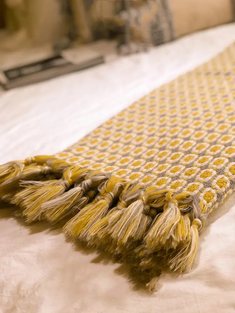 a soft mustard-yellow and gray woven cover blanket knitted with a repeating geometric pattern and fringed edges suitable as a sofa blanket cover